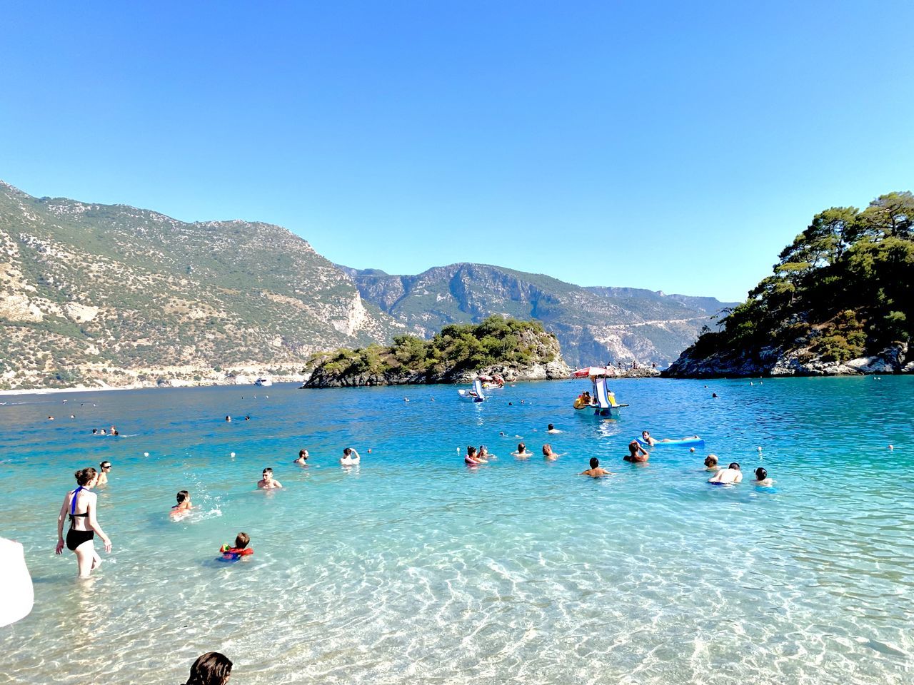 PEOPLE SWIMMING IN SEA AGAINST CLEAR SKY