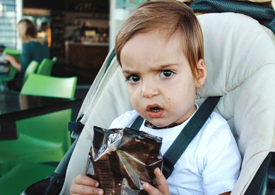 Portrait of cute toddler sitting in pram holding a packet of crisps