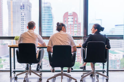 Rear view of business people sitting on chairs at table by window