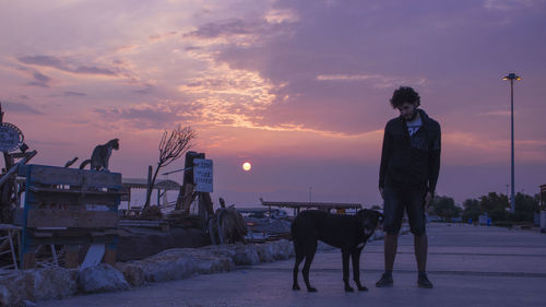 People standing with dog against sky during sunset