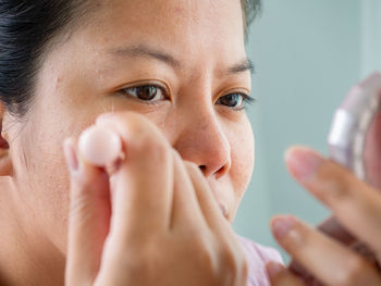 Close-up of woman applying makeup against wall
