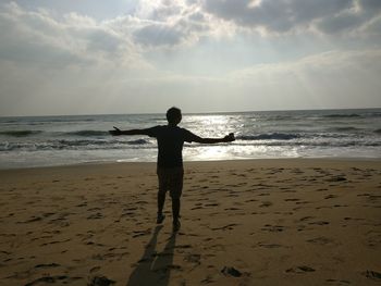 Rear view of silhouette boy on beach against sky