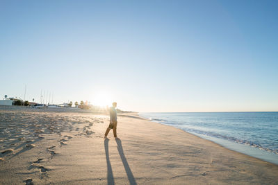 Rear view of woman standing on beach against clear sky