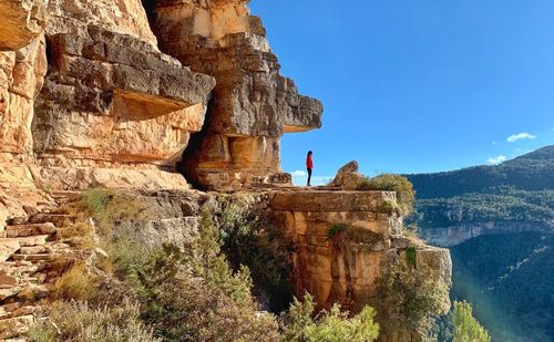 Side view of woman standing on cliff against blue sky