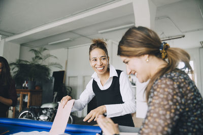 Smiling businesswoman looking at female colleague while working in creative office