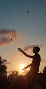 Silhouette man flying against sky during sunset