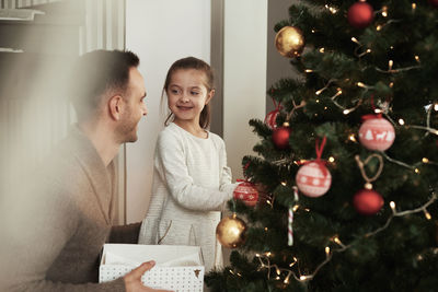 Girl standing with father by christmas tree at home
