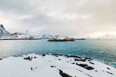 Scenic view of sea by snowcapped mountains against sky