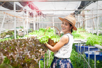 Side view of a smiling young woman standing in greenhouse