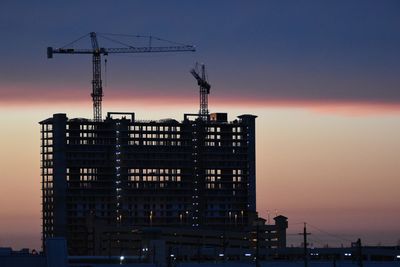 Evening view of tall building being constructed with colorful horizon in background