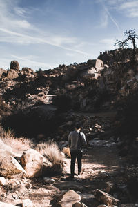 Rear view of man standing on cliff against sky