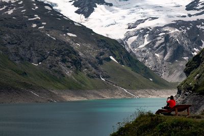 Rear view of man sitting on shore against mountain