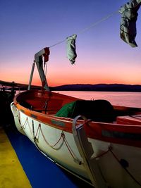 Fishing boat moored in sea against sky during sunset