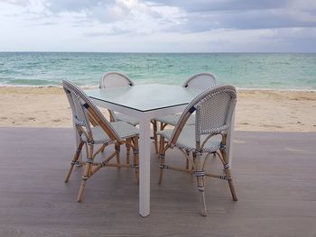 Chair on table by sea against sky