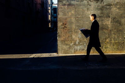 Side view of businessman reading newspaper while walking on sidewalk
