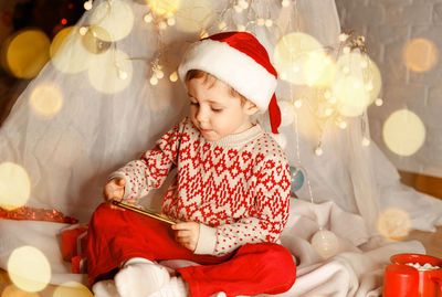 Cute boy using mobile phone while sitting at home during christmas