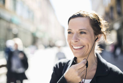 Smiling mature businesswoman talking through headphones on city street