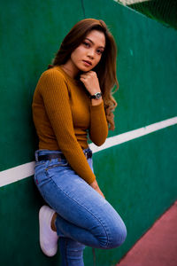 Portrait of young woman standing by green wall