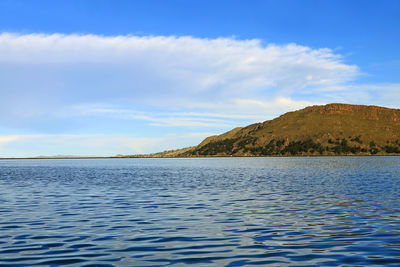 Scenic view of sea by mountain against sky