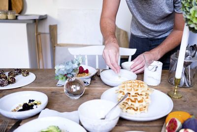 Midsection of man garnishing yogurt in plate at wooden table