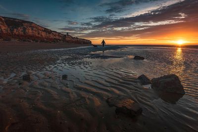 Silhouette woman walking against sea during sunset