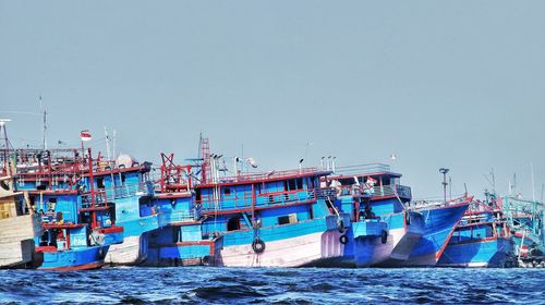 Fishing boats moored at harbor against clear sky