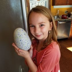 Portrait of smiling girl holding easter egg in kitchen at home
