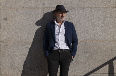 Portrait of adult man in hat and suit standing on street against wall. madrid, spain