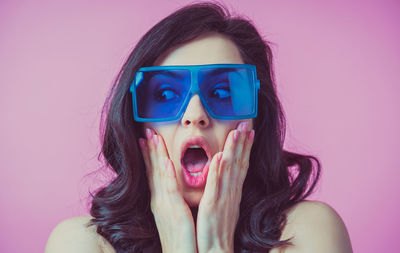 Close-up of young woman wearing sunglasses against pink background