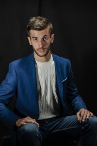 Portrait of young man sitting against black background