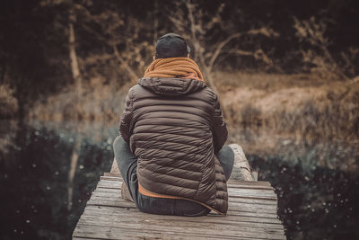 Rear view of man sitting on wood against trees