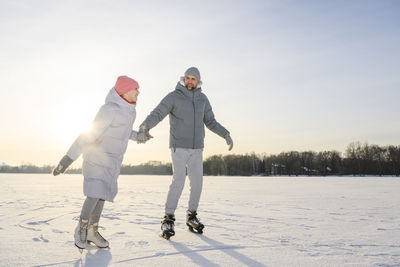 Happy daughter with father practicing ice skating on winter lake