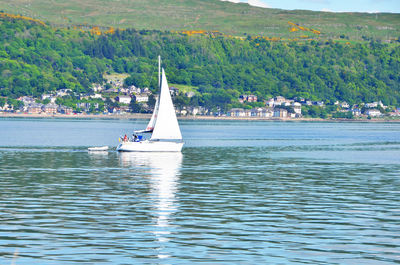 Sailboat sailing on sea by mountain against sky