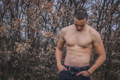 Shirtless young man standing against trees