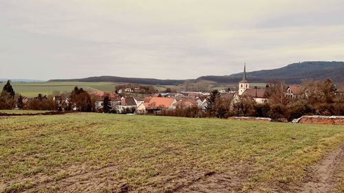 Scenic view of field by houses against sky