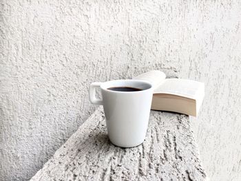 Close-up of coffee cup and book on retaining wall