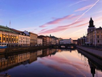 Bridge over river by buildings against sky at sunset