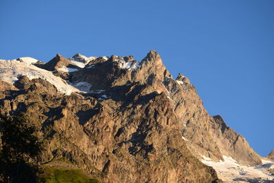 Low angle view of rocky mountains against clear blue sky