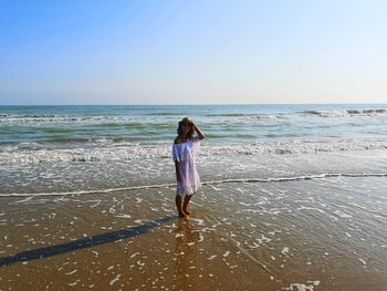 Rear view of woman standing on beach against sky