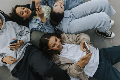 High angle view of smiling teenagers lying together and using their phones