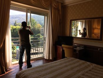 Rear view of man looking through window at home