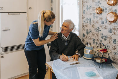 Female care assistant talking to senior man doing soduko at home