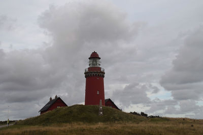 Lighthouse amidst buildings against cloudy sky