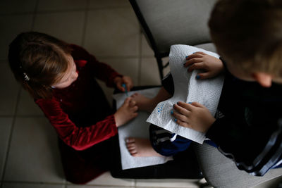 High angle view of sister painting brother's toenails sitting on chair at home