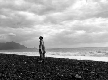 Side view of mid adult man standing at beach against cloudy sky