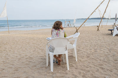 Rear view of woman sitting on chair at beach