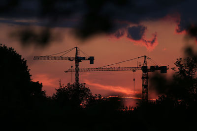 Silhouette of cranes against sky during sunset