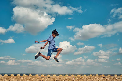 Low angle view of boy jumping against sky