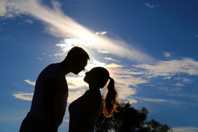 Side view of silhouette couple standing face to face against sky during sunset