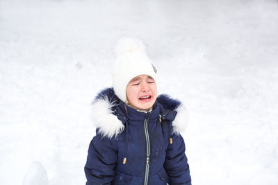 Little girl crying outside in winter. a child in warm clothes is upset, cold, wipes away tears, 